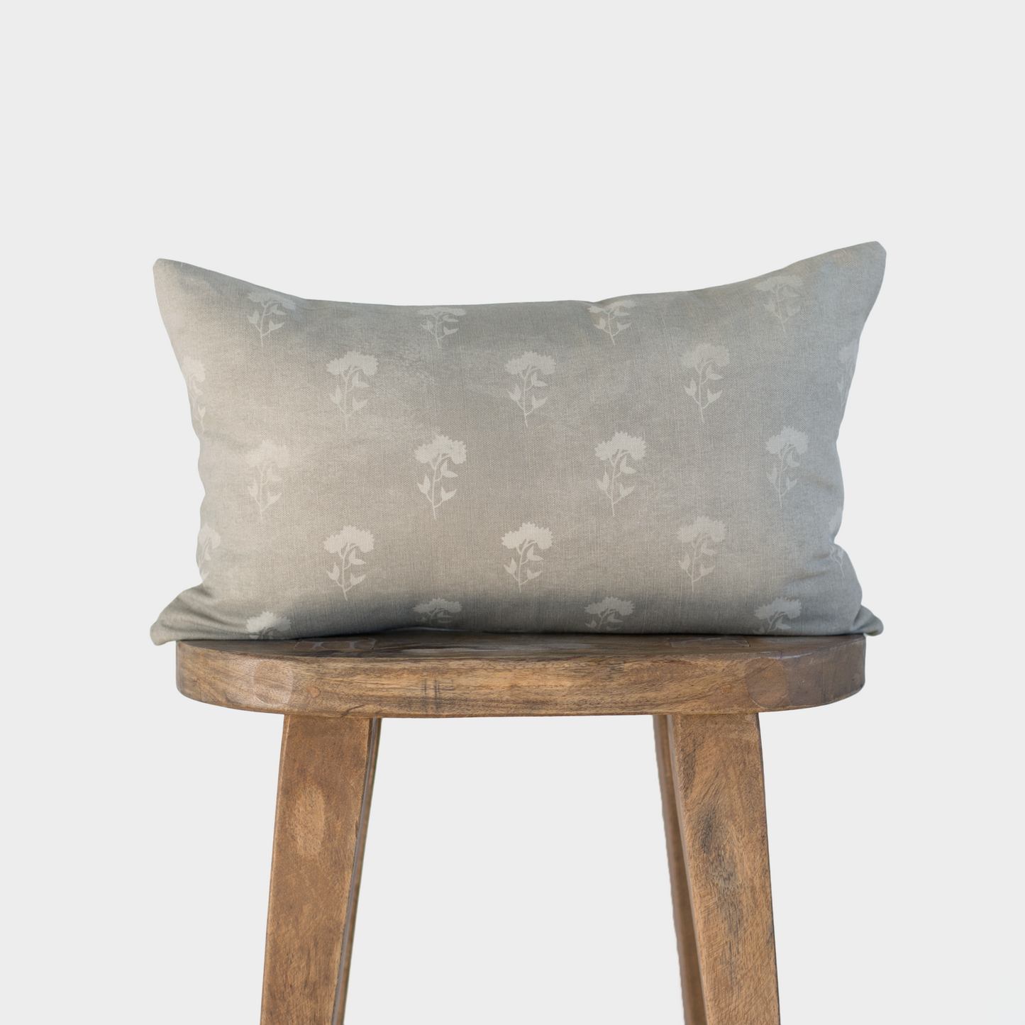 Gray lumbar pillow with white floral pattern displayed on wooden stool.