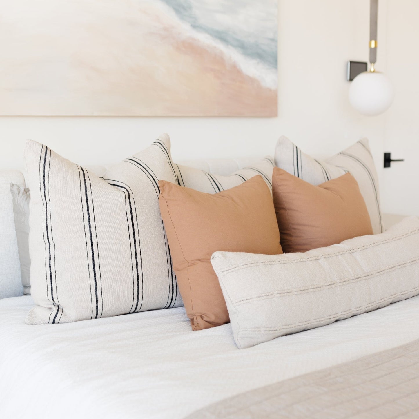 Striped and solid tan pillows arranged on a white bed with matching lumbar pillow.