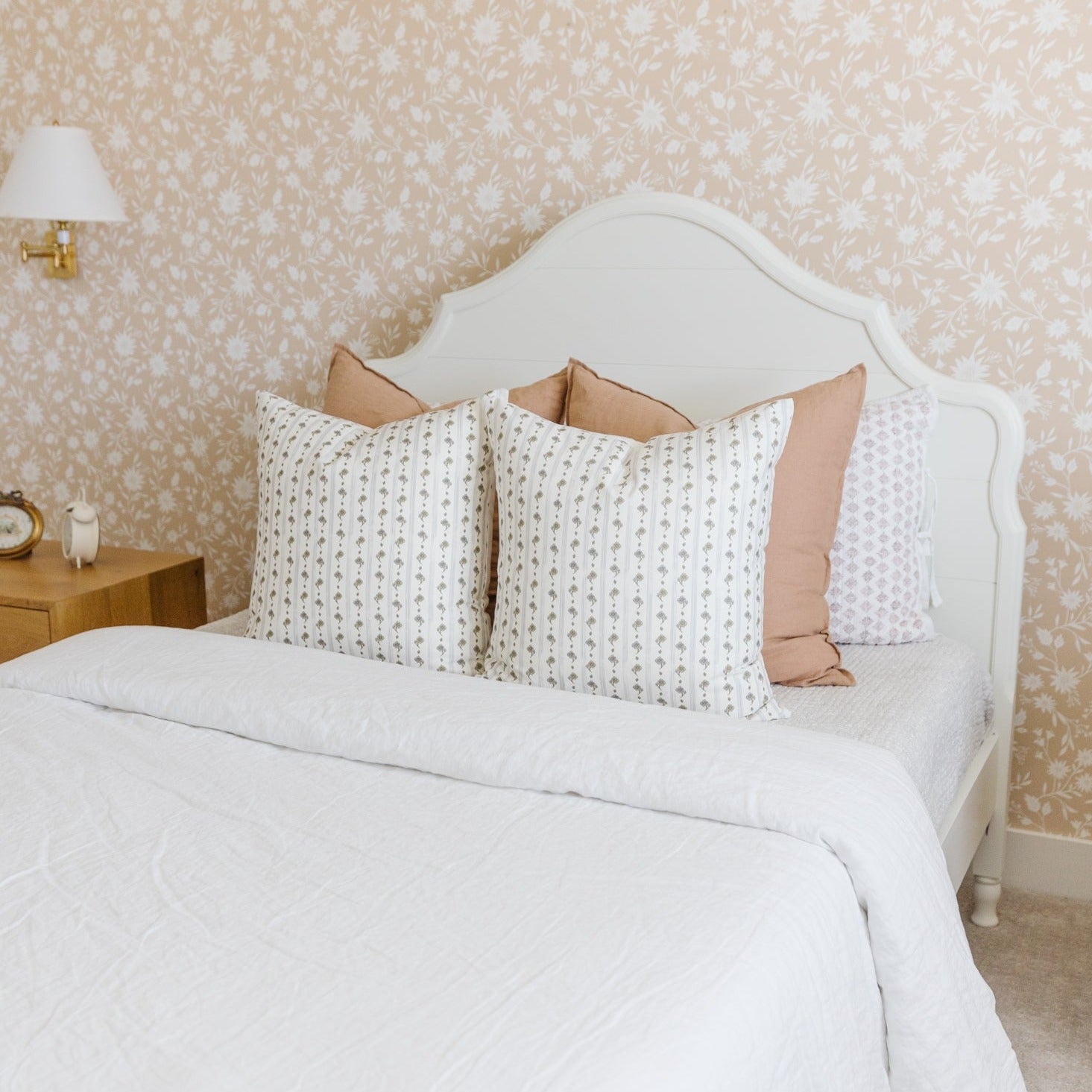 Cream and white striped pillow with small floral pattern displayed on bed with white headboard.