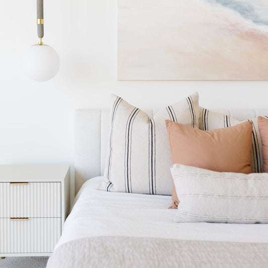 Bedroom styled with white bedding, striped and terracotta pillows, pendant light, and nightstand.