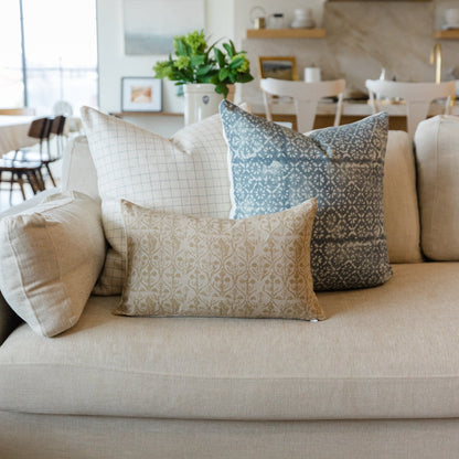 Rectangular pillow with tan floral damask pattern displayed on beige sofa with coordinating patterned pillows.