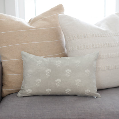 Gray lumbar pillow with cream floral pattern, displayed among coordinating neutral pillows on a sofa.