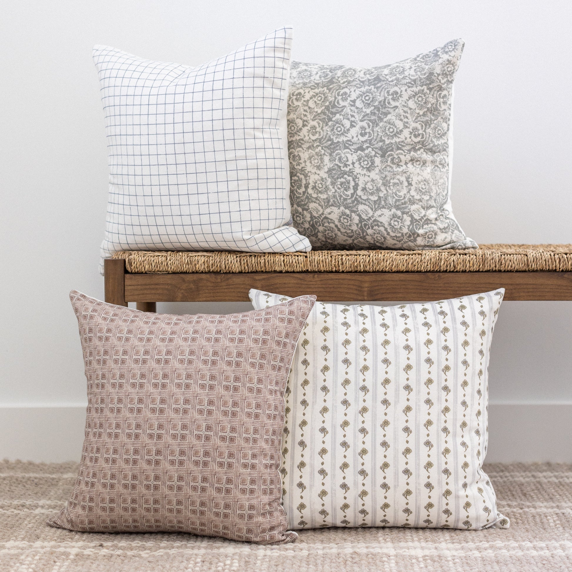 Four decorative throw pillows with grid, damask, geometric, and vertical stripe patterns in neutral tones.