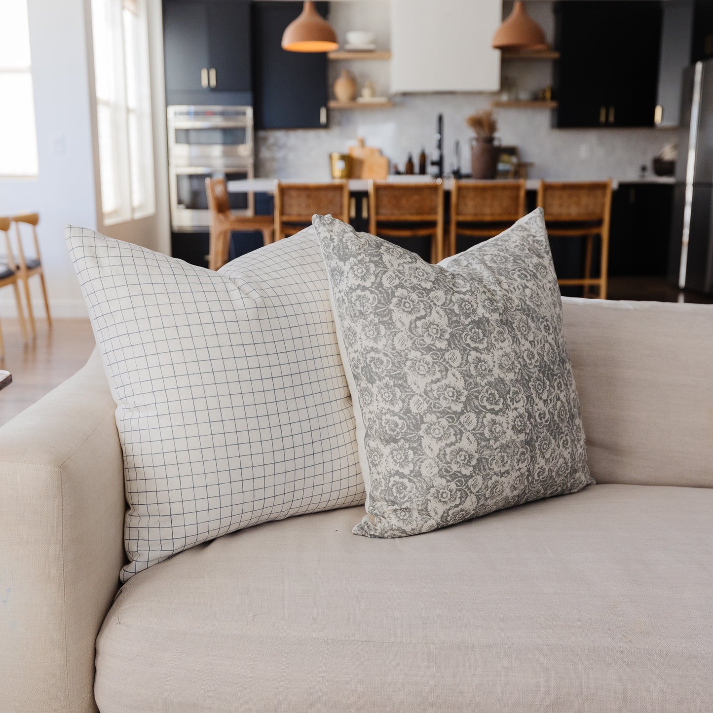 Two gray and white patterned throw pillows on a beige sofa, one with grid print and one with floral damask design.