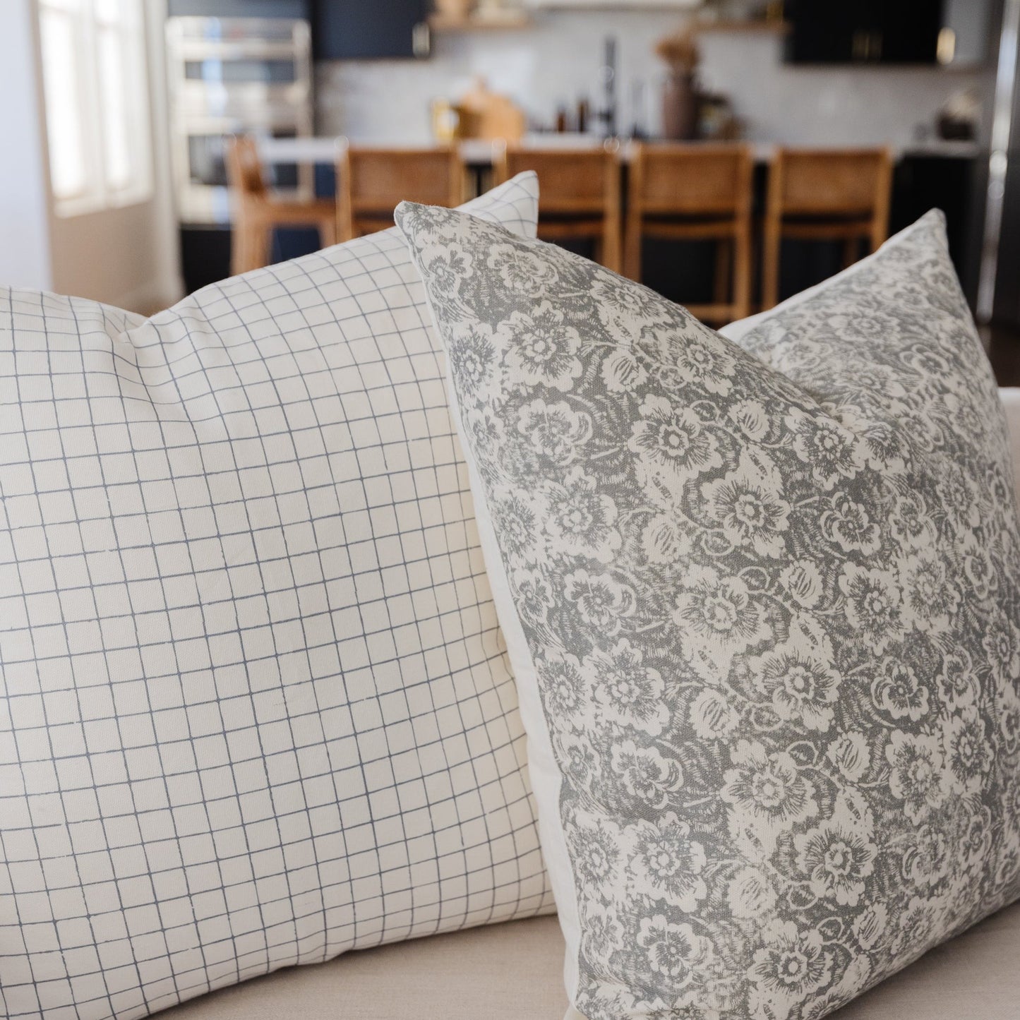 Two gray and cream patterned throw pillows, one with floral damask print and one with grid pattern, displayed on a sofa.