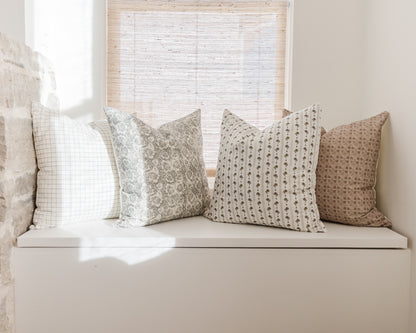 Four patterned throw pillows in neutral tones with grid, floral, striped, and geometric designs arranged on a white window se