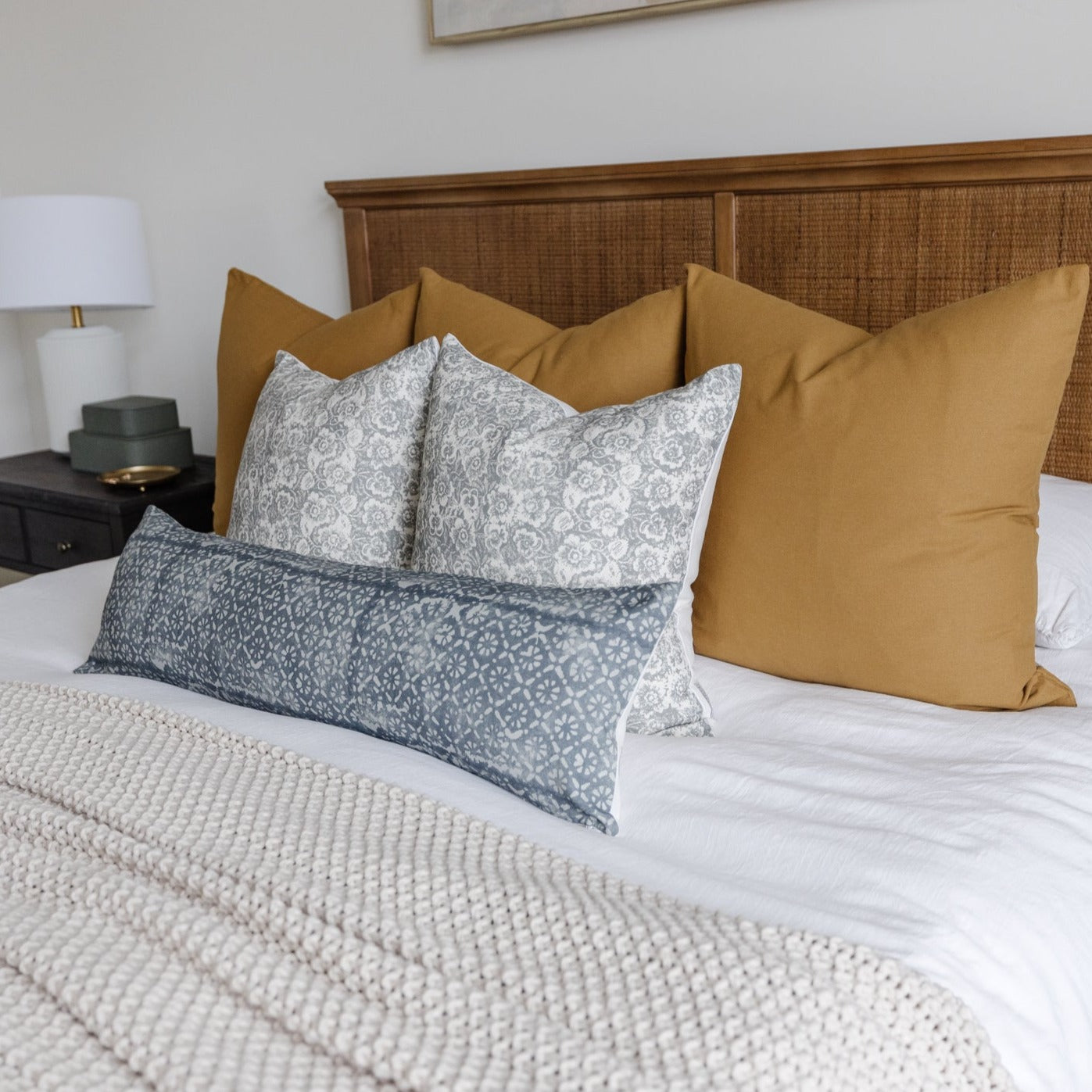 Rectangular lumbar pillow with gray diamond floral pattern displayed on bed with solid mustard pillows.
