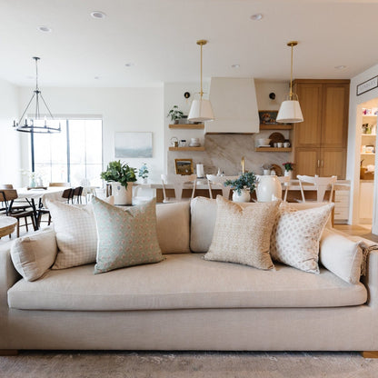 Cream pillow cover with hourglass-shaped floral pattern in muted tones, displayed on beige sofa.