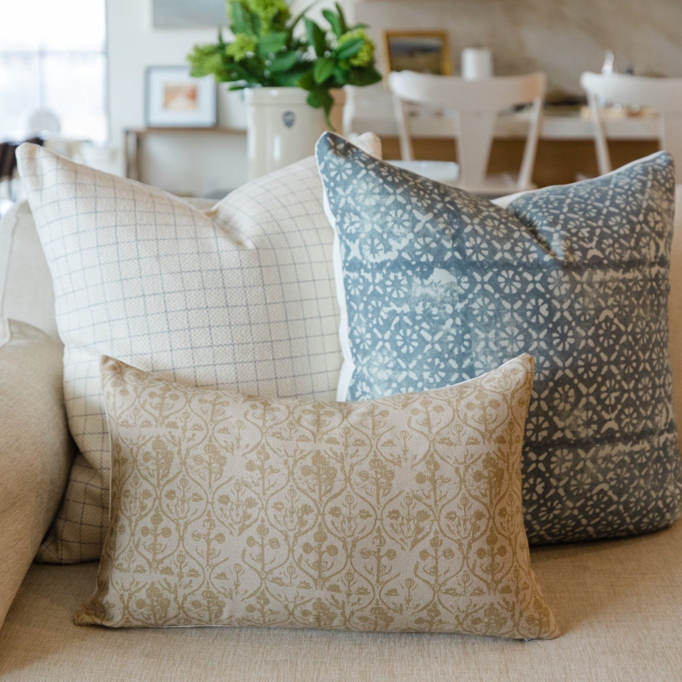 Decorative pillows with diamond floral patterns in blue, tan, and cream on neutral sofa.