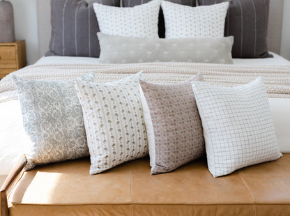 Four decorative pillows in neutral tones with floral, dotted, textured, and grid patterns displayed on a bed.