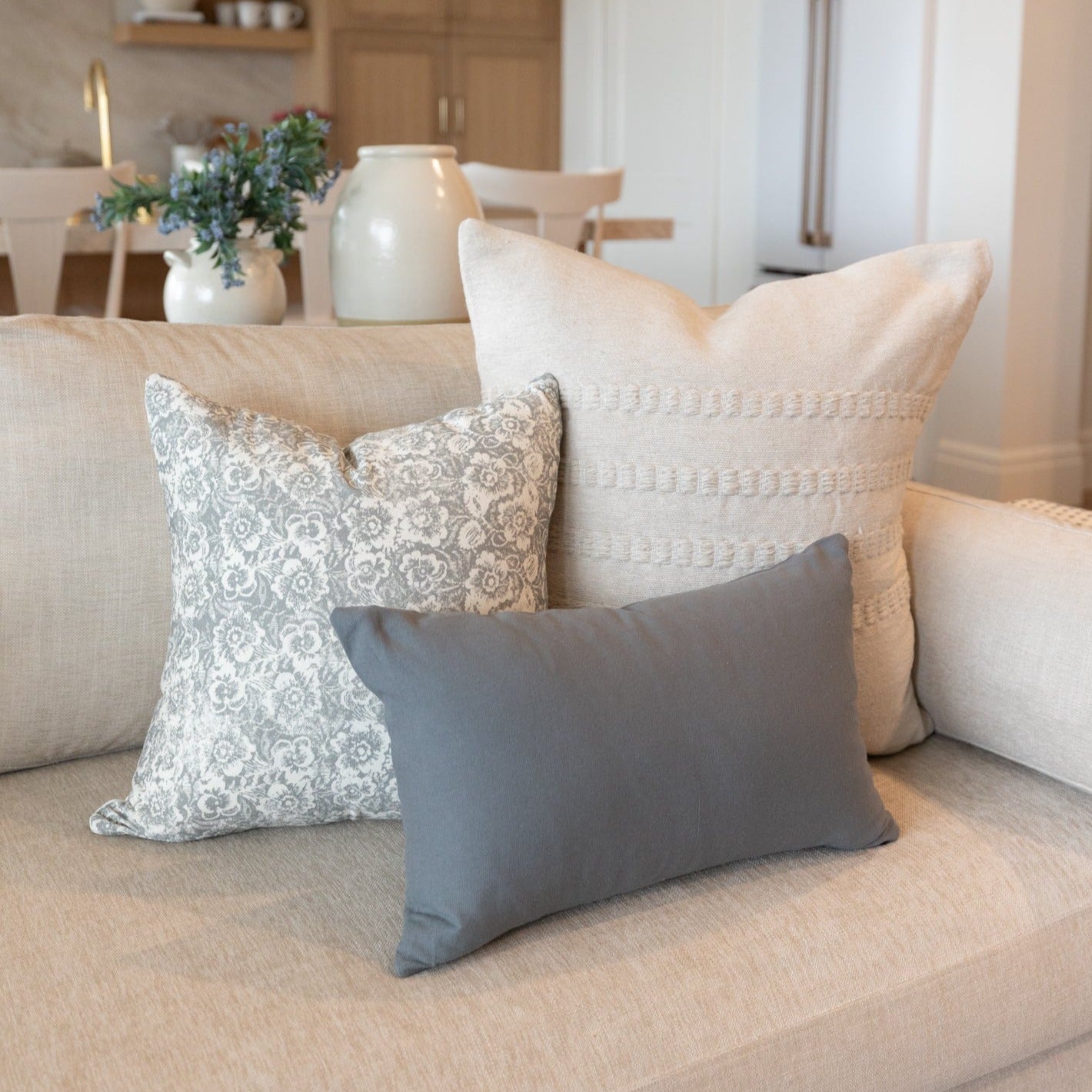 Gray rectangular throw pillow displayed on a beige sofa with patterned and textured pillows.