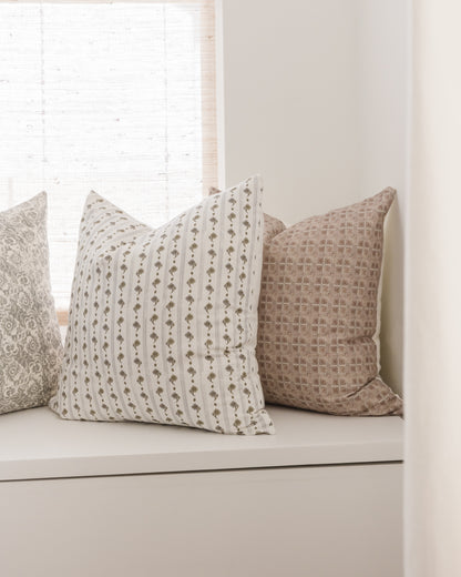 Four decorative pillows in neutral tones with geometric and textured patterns, displayed on a white shelf.
