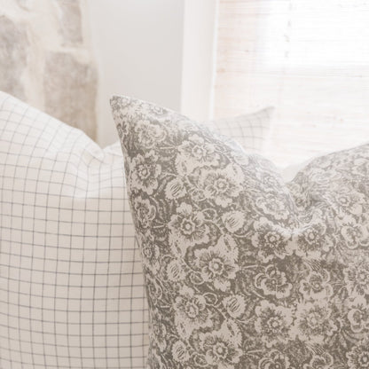 Gray and cream floral patterned pillow with coordinating grid-patterned pillow beside it.