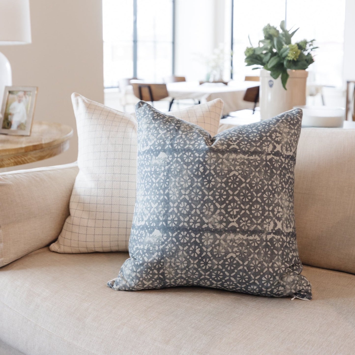 Gray and white diamond floral patterned pillow on beige sofa next to grid-pattern pillow.