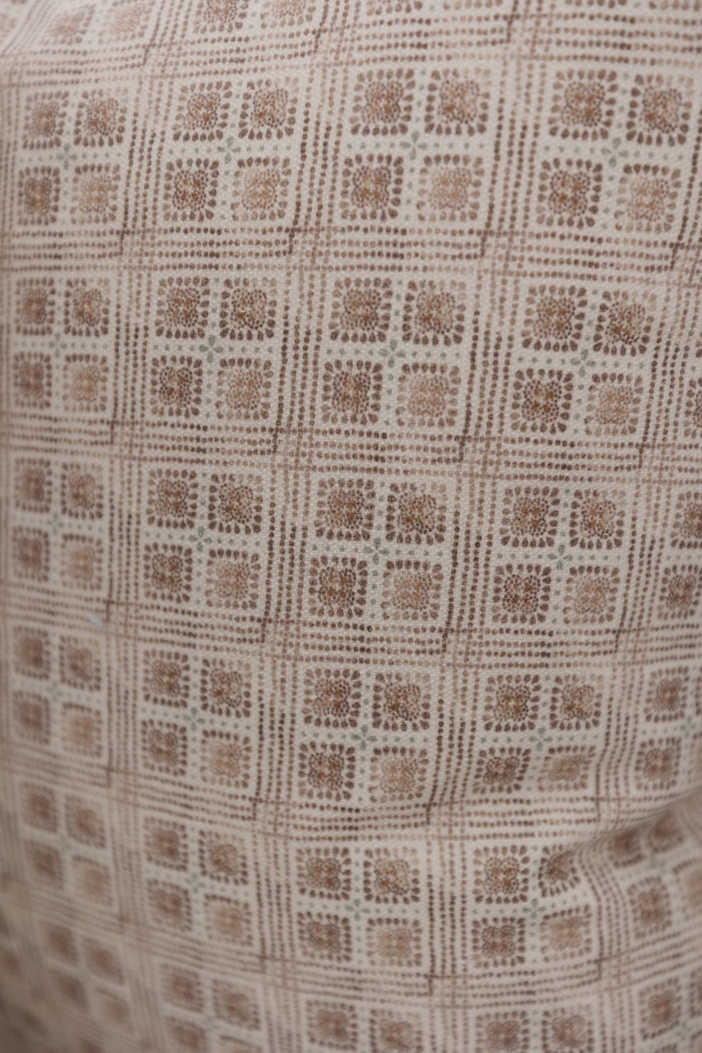 Brown and cream woven fabric with a repeating floral grid pattern in dotted texture.