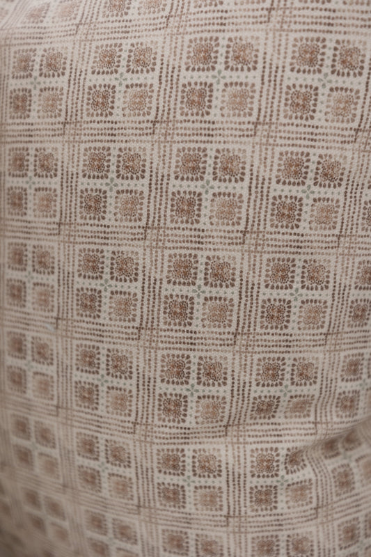 Brown and cream woven fabric with a repeating floral grid pattern in dotted texture.