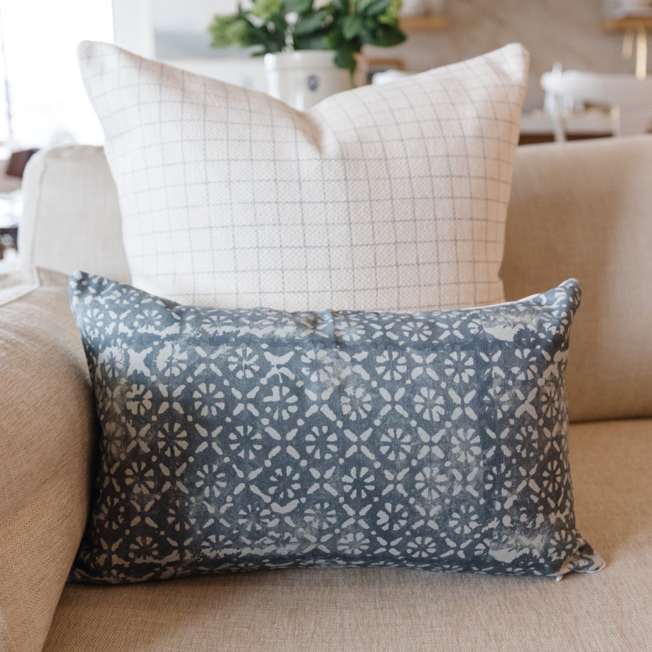 Blue-gray lumbar pillow with repeating white diamond and floral pattern, displayed on a beige sofa.
