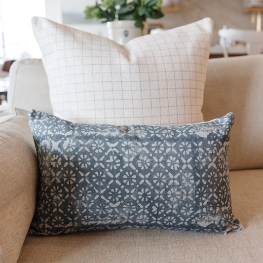 Blue-gray lumbar pillow with repeating white diamond and floral pattern, displayed on a beige sofa.