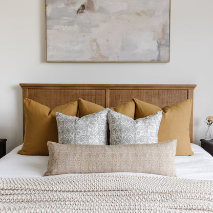 Rectangular lumbar pillow with beige geometric floral pattern displayed on bed with coordinating gold and patterned pillows.
