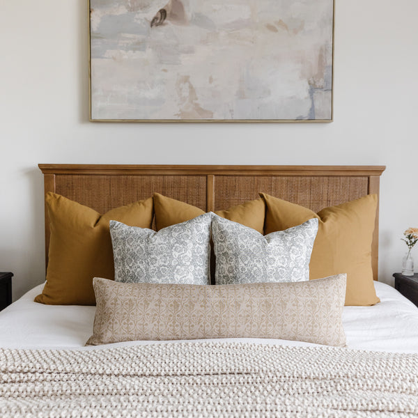 Rectangular lumbar pillow with beige geometric floral pattern displayed on bed with coordinating gold and patterned pillows.