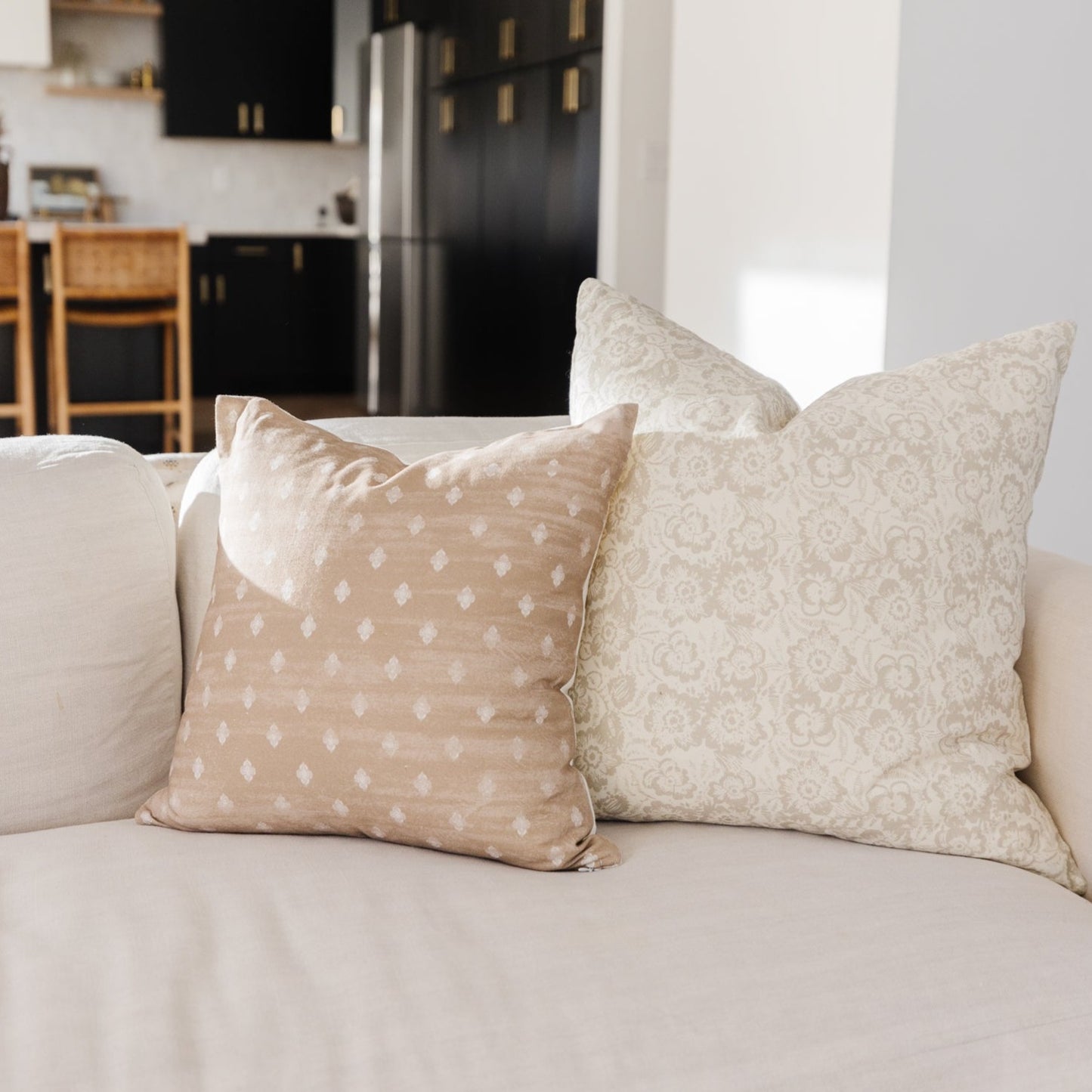 Beige pillow covers with white geometric patterns displayed on a cream sofa in a modern living room setting.