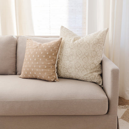 Beige and cream pillow covers with floral and dot patterns displayed on a light gray sofa.