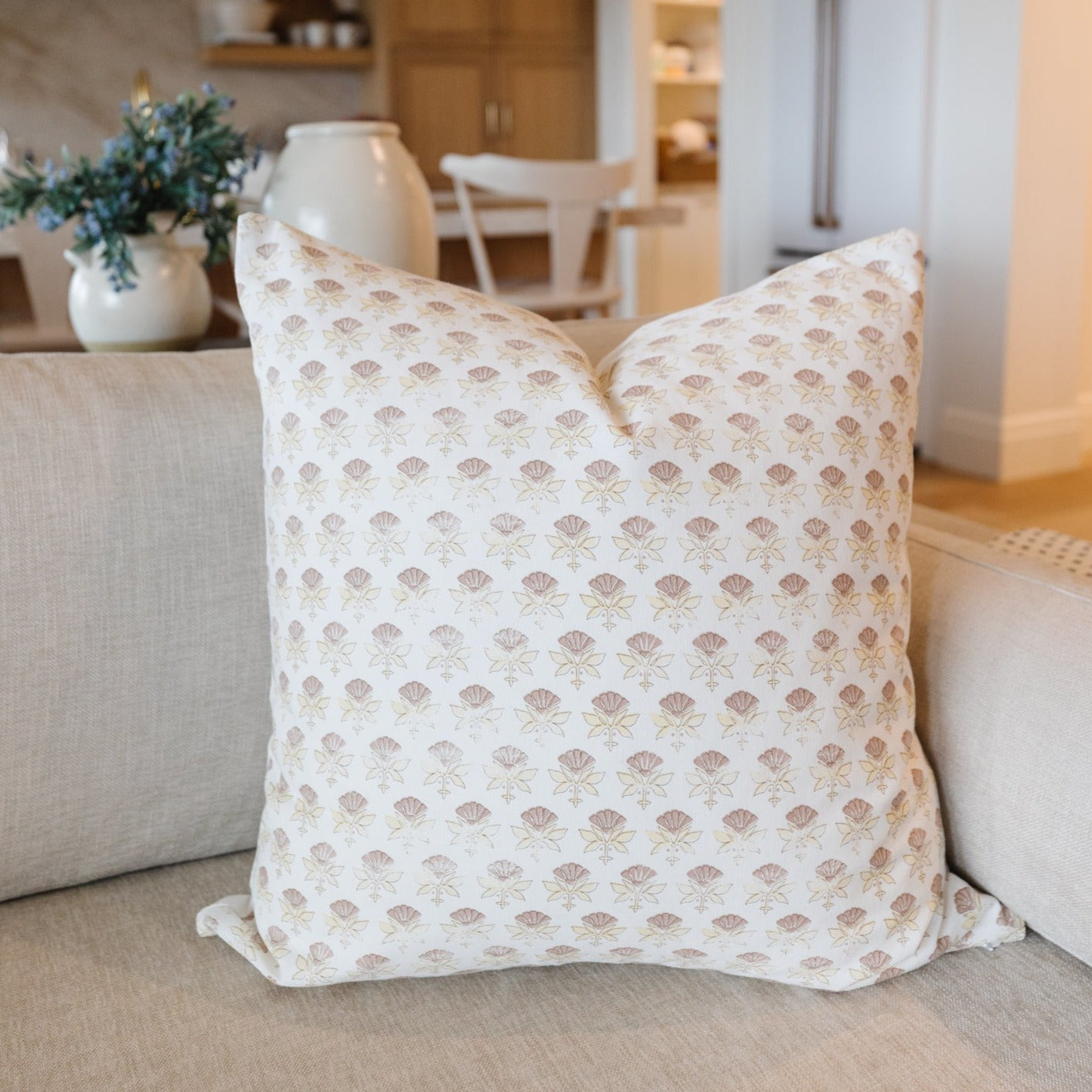 White throw pillow with all-over tan floral fan pattern, displayed on beige sofa.