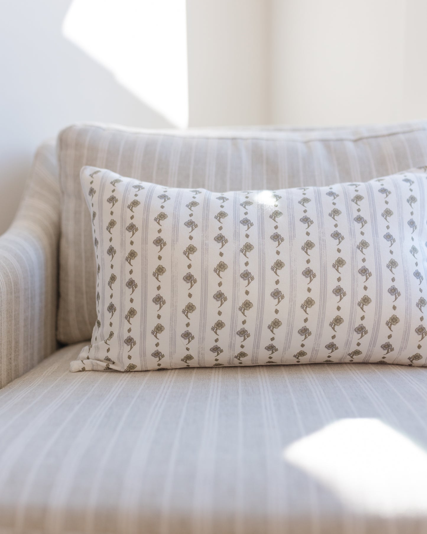 Rectangular lumbar pillow with small taupe floral motifs arranged in vertical stripes on cream background.