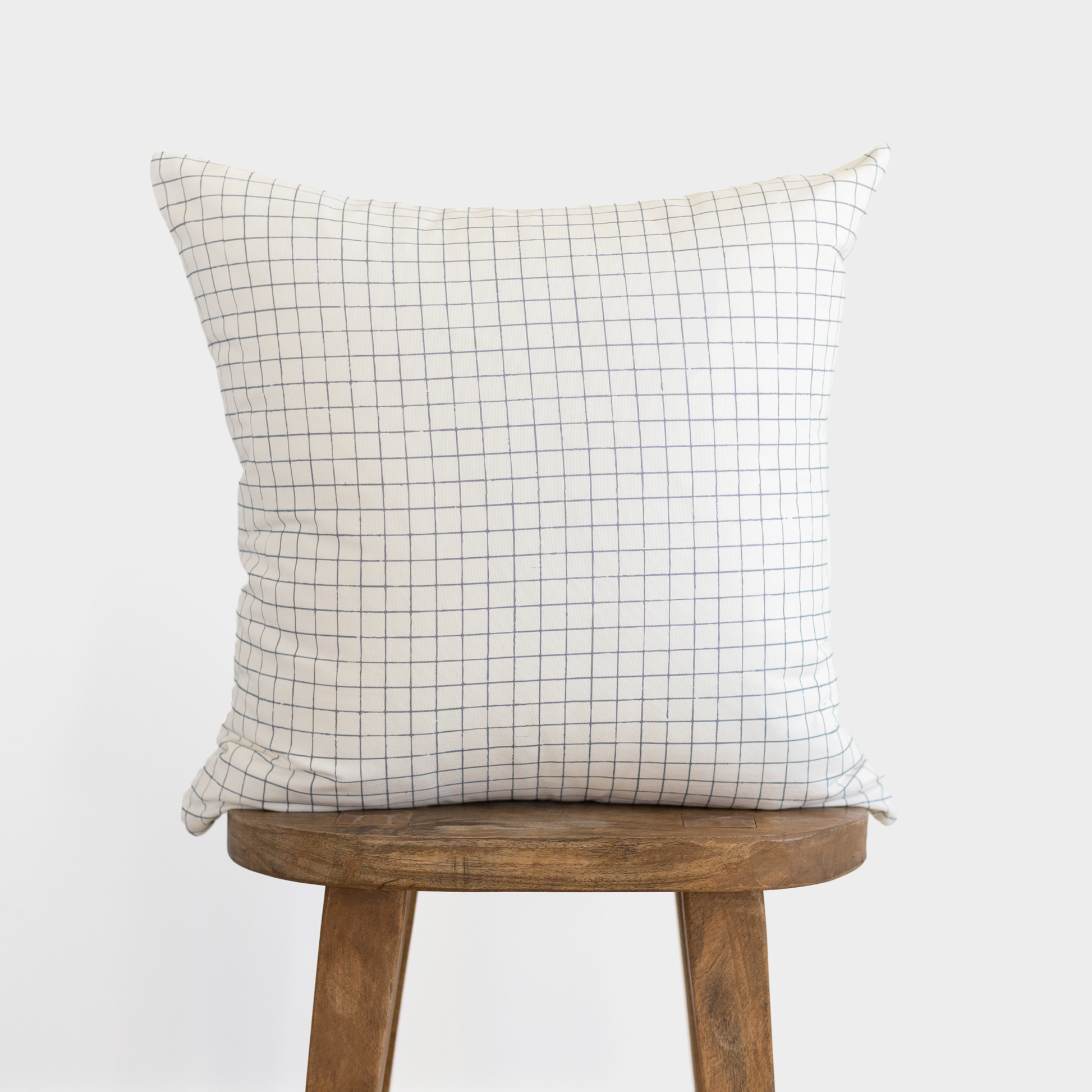 Cream pillow cover with small grid pattern displayed on wooden stool.