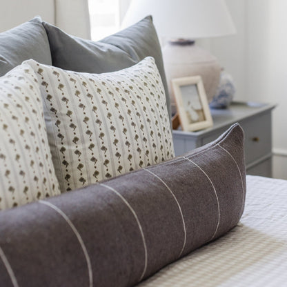 18" pillow with cream background and small tan floral print, displayed with gray striped pillows on a bed.