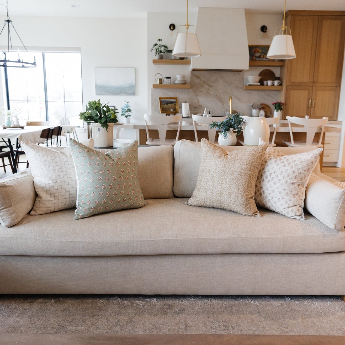 Four decorative pillows in neutral tones with geometric and floral patterns arranged on a beige sofa.