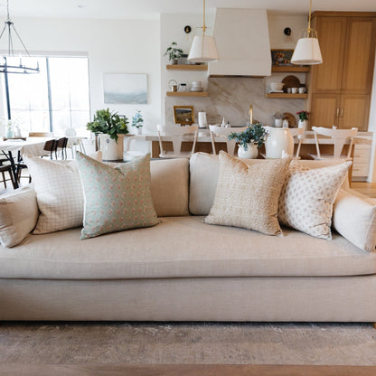 Four decorative pillows in neutral tones with geometric and floral patterns arranged on a beige sofa.