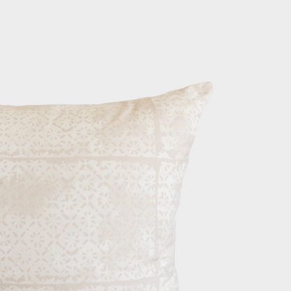 Cream-colored pillow with faded floral pattern and visible seam detail against light background.