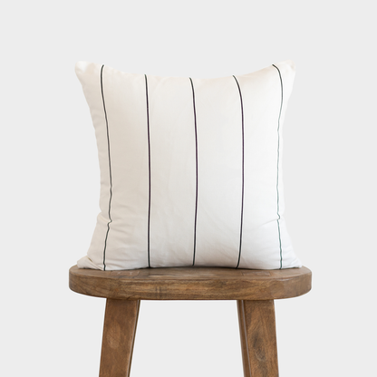 Cream pillow with evenly spaced black vertical pin stripes, displayed on a wooden stool.