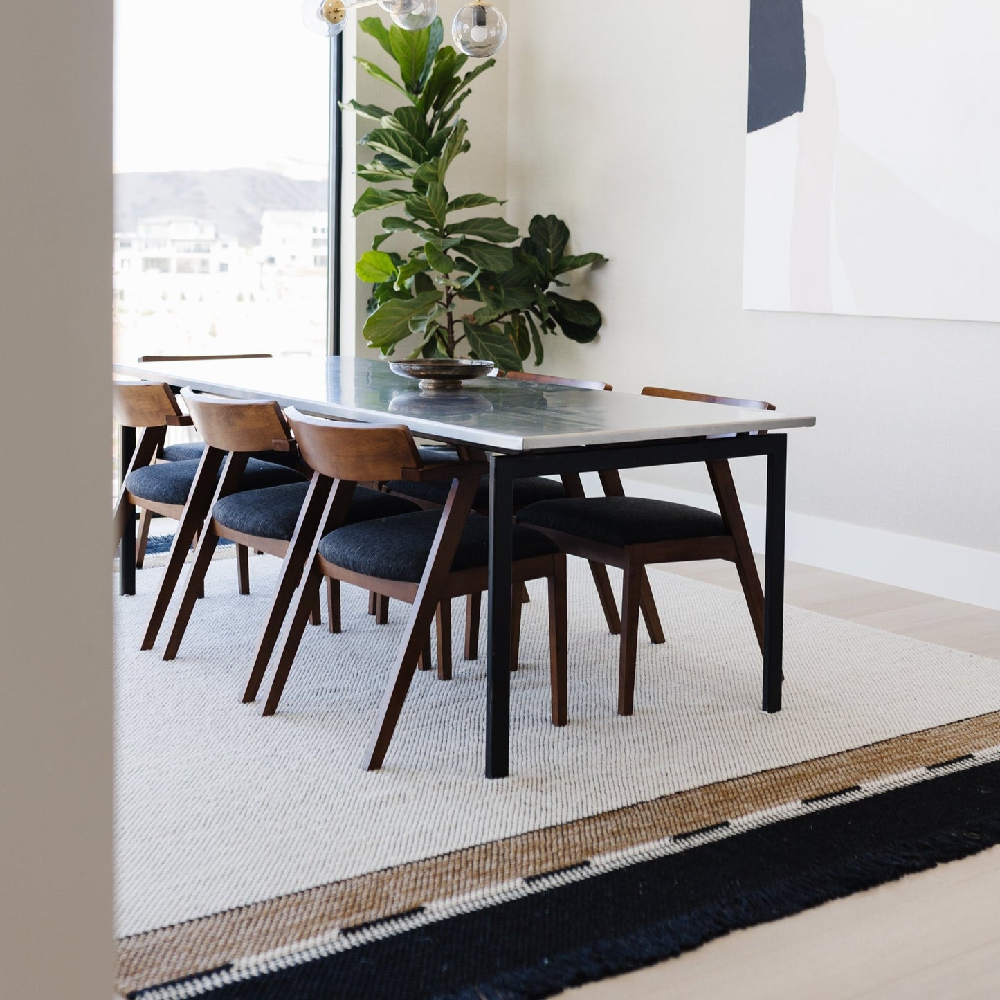 Modern dining table with black top and wooden legs, paired with four mid-century chairs upholstered in navy blue.