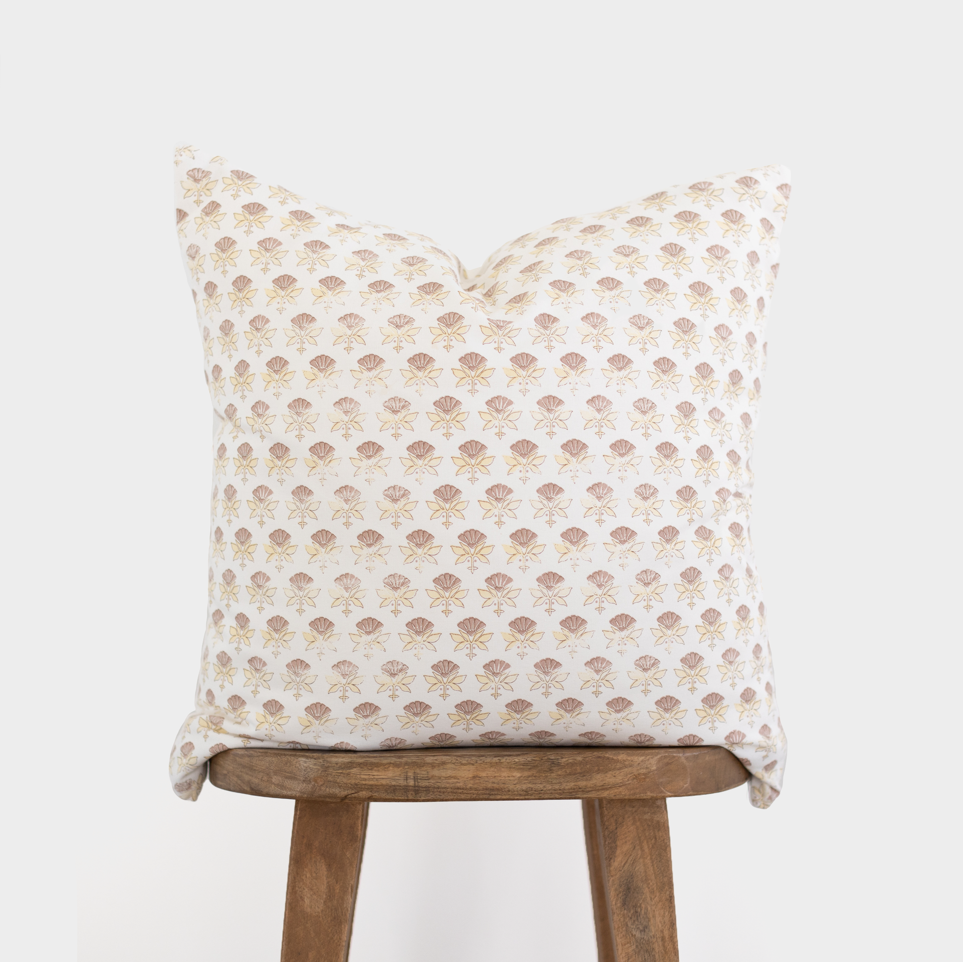 White pillow with an all-over tan floral fan pattern displayed on a wooden stool.