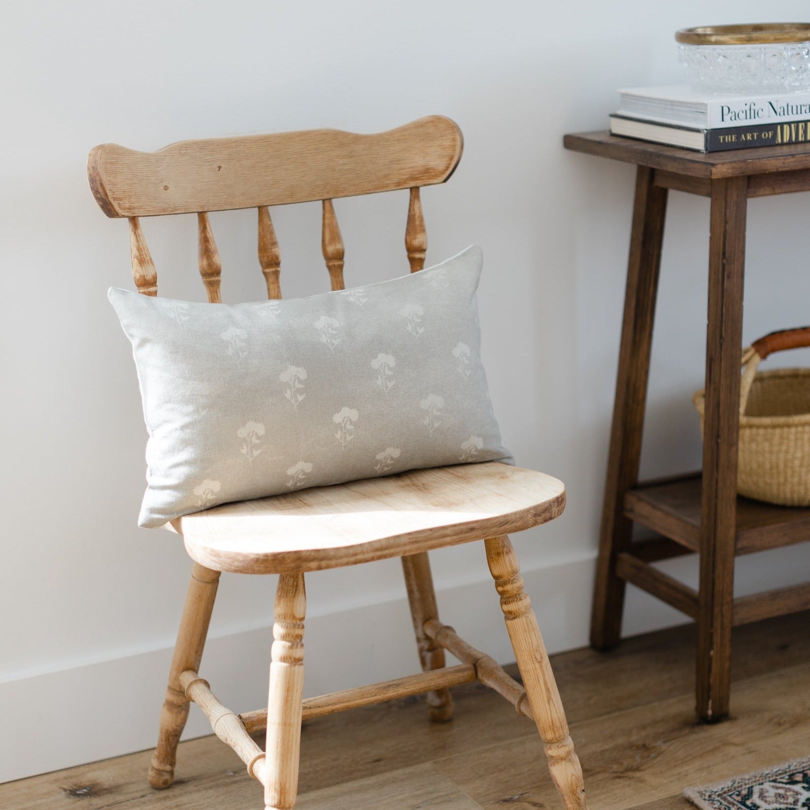 Gray lumbar pillow with cream floral pattern displayed on wooden chair.