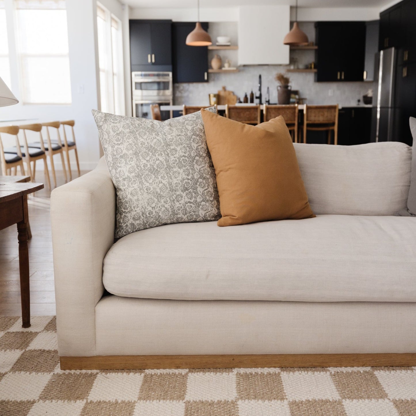 Gray floral patterned throw pillow on cream sofa with tan solid pillow beside it.