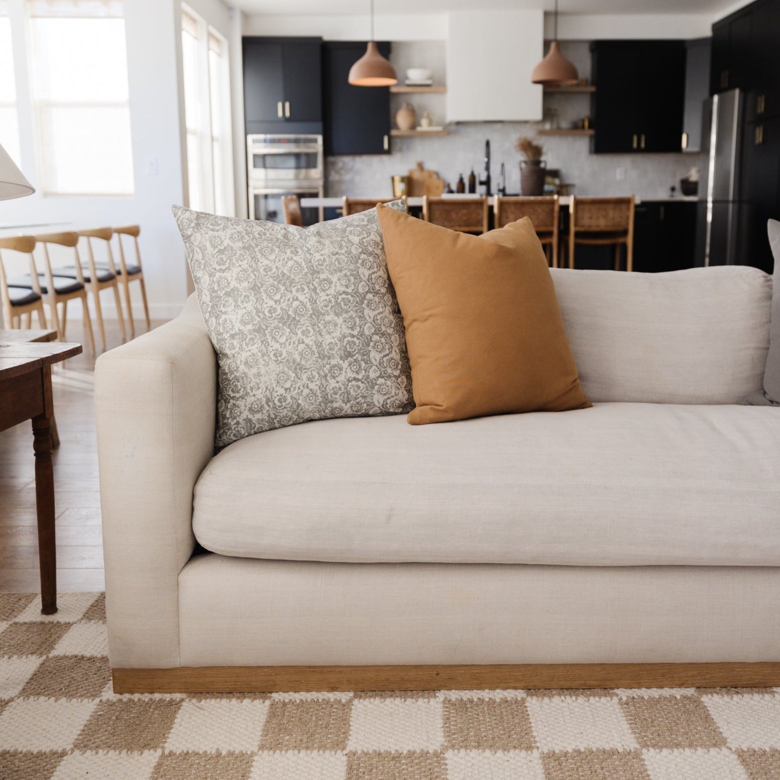 Gray floral patterned throw pillow on cream sofa with tan solid pillow beside it.