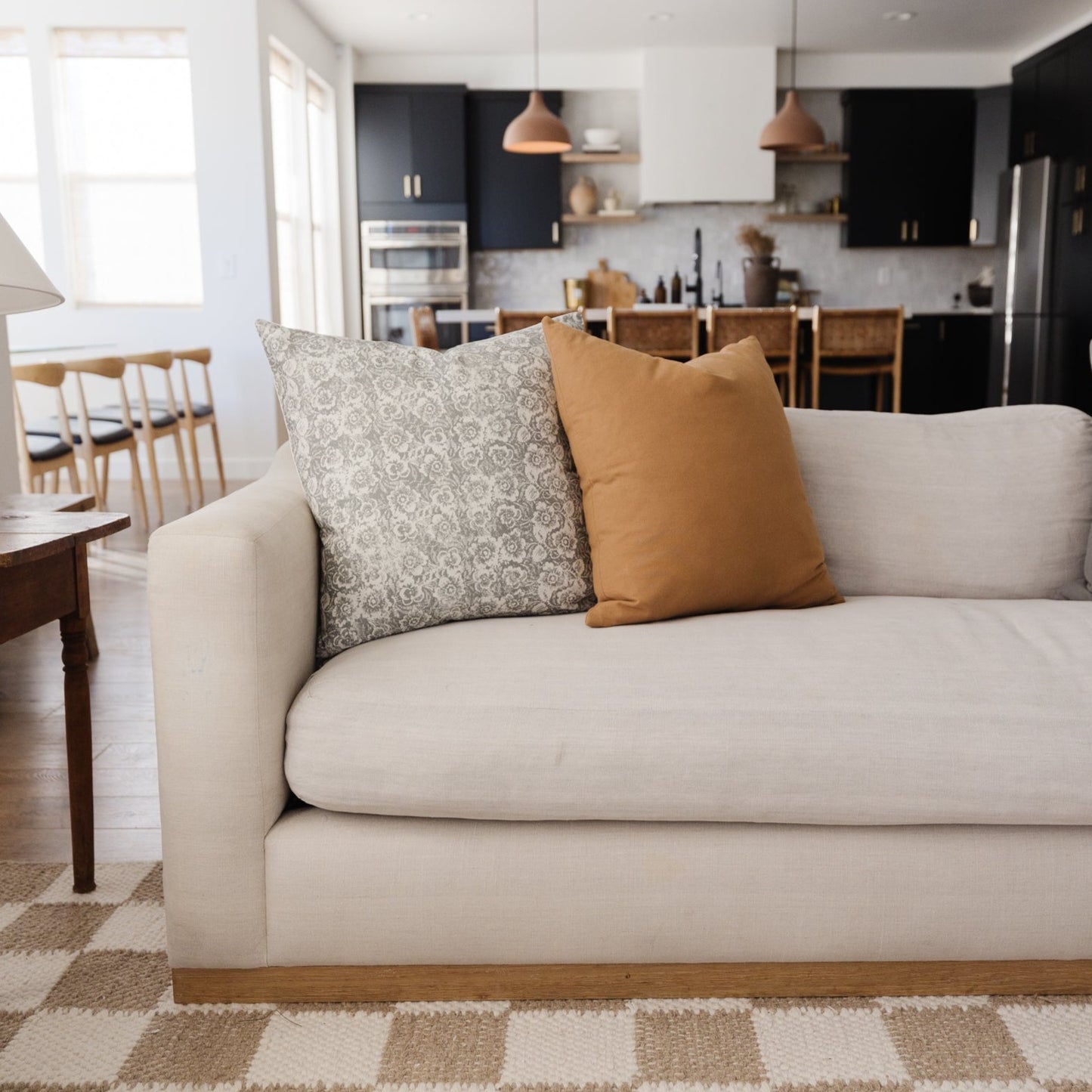 Terracotta Basics throw pillow in solid tan displayed on cream sofa with patterned pillow.