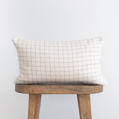 Cream lumbar pillow with gray grid pattern on wooden stool.