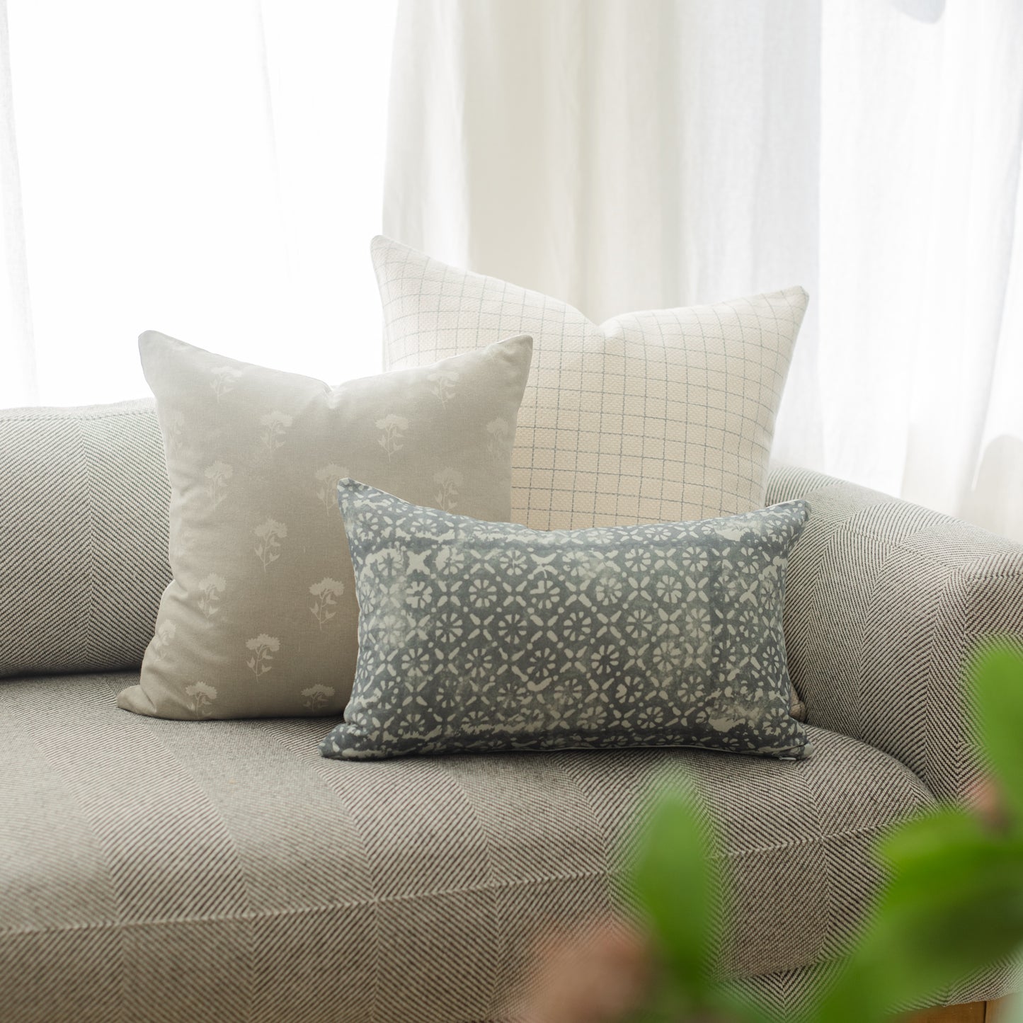 Three decorative pillows with geometric and floral patterns arranged on a gray upholstered sofa near a window.