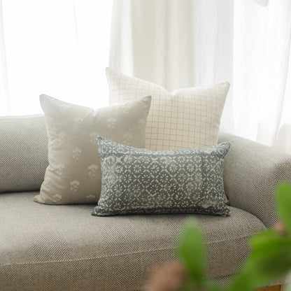 Three decorative pillows with geometric and floral patterns arranged on a gray upholstered sofa near a window.