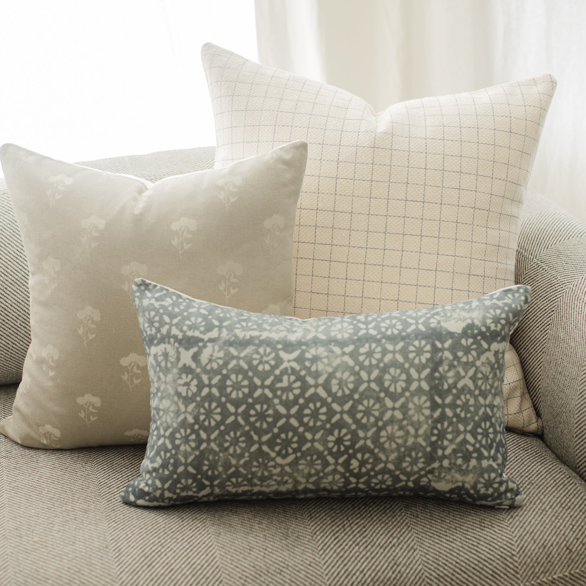 Rectangular lumbar pillow with teal and cream geometric damask pattern on a gray upholstered surface.