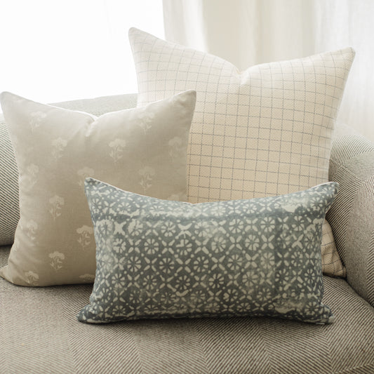 Rectangular lumbar pillow with teal and cream geometric damask pattern on a gray upholstered surface.