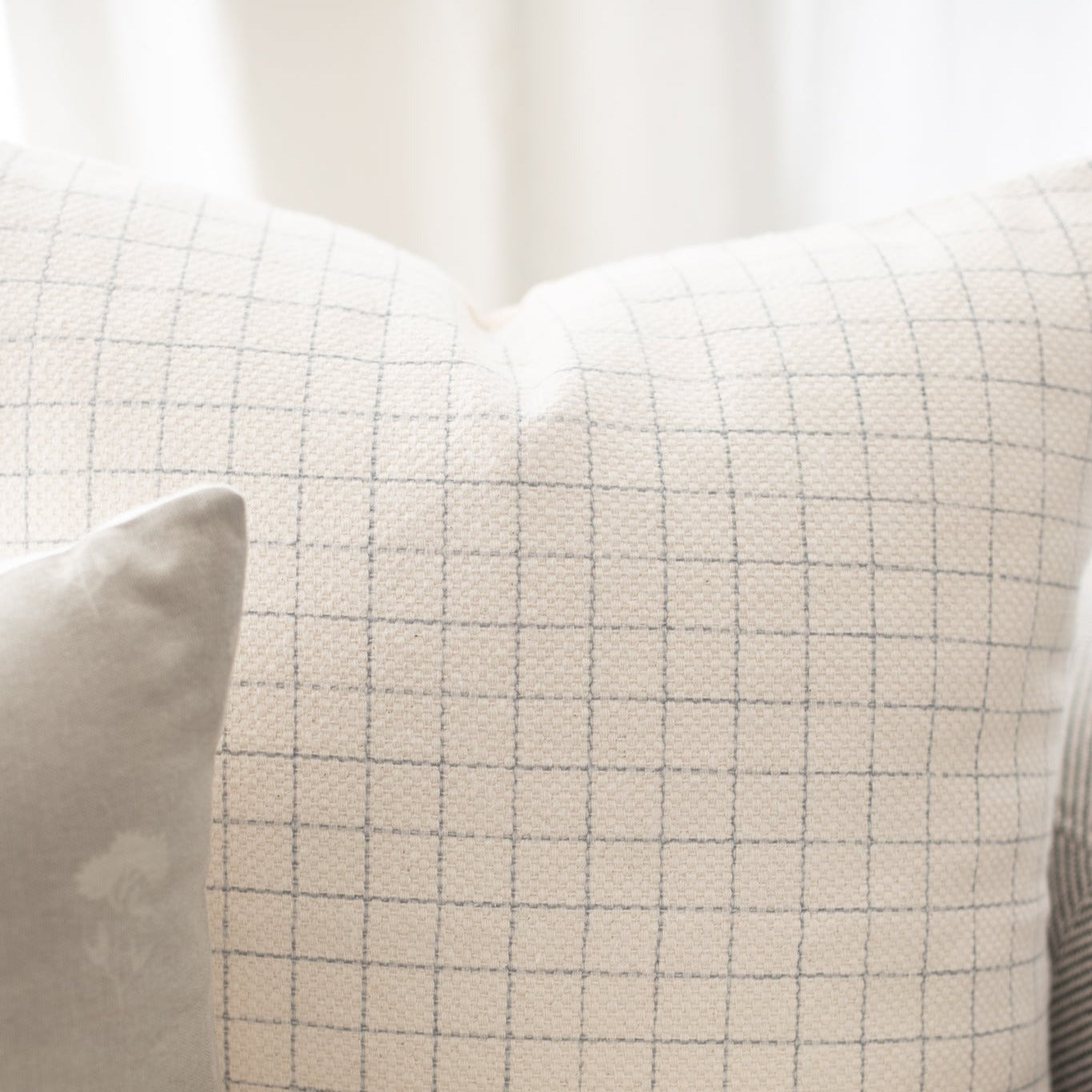 Cream-colored pillow with gray grid pattern and white piping detail.