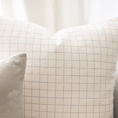 Cream-colored pillow with gray grid pattern and white piping detail.