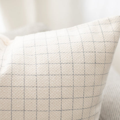 Cream linen pillow with gray grid pattern and white piping along the edge.