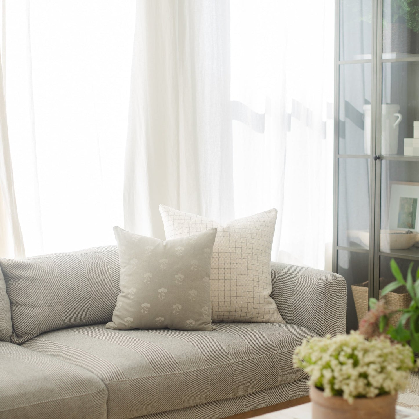 Cream-colored square pillow with grid pattern displayed on gray sofa near window.