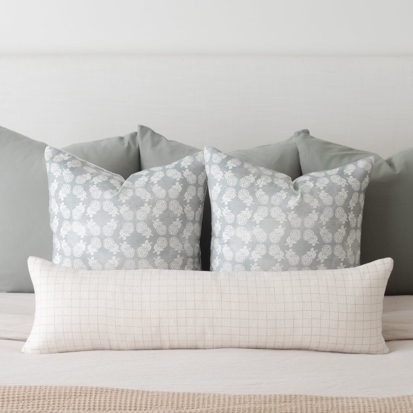 Cream-colored lumbar pillow with fine grid pattern, displayed with two gray patterned pillows on a bed.